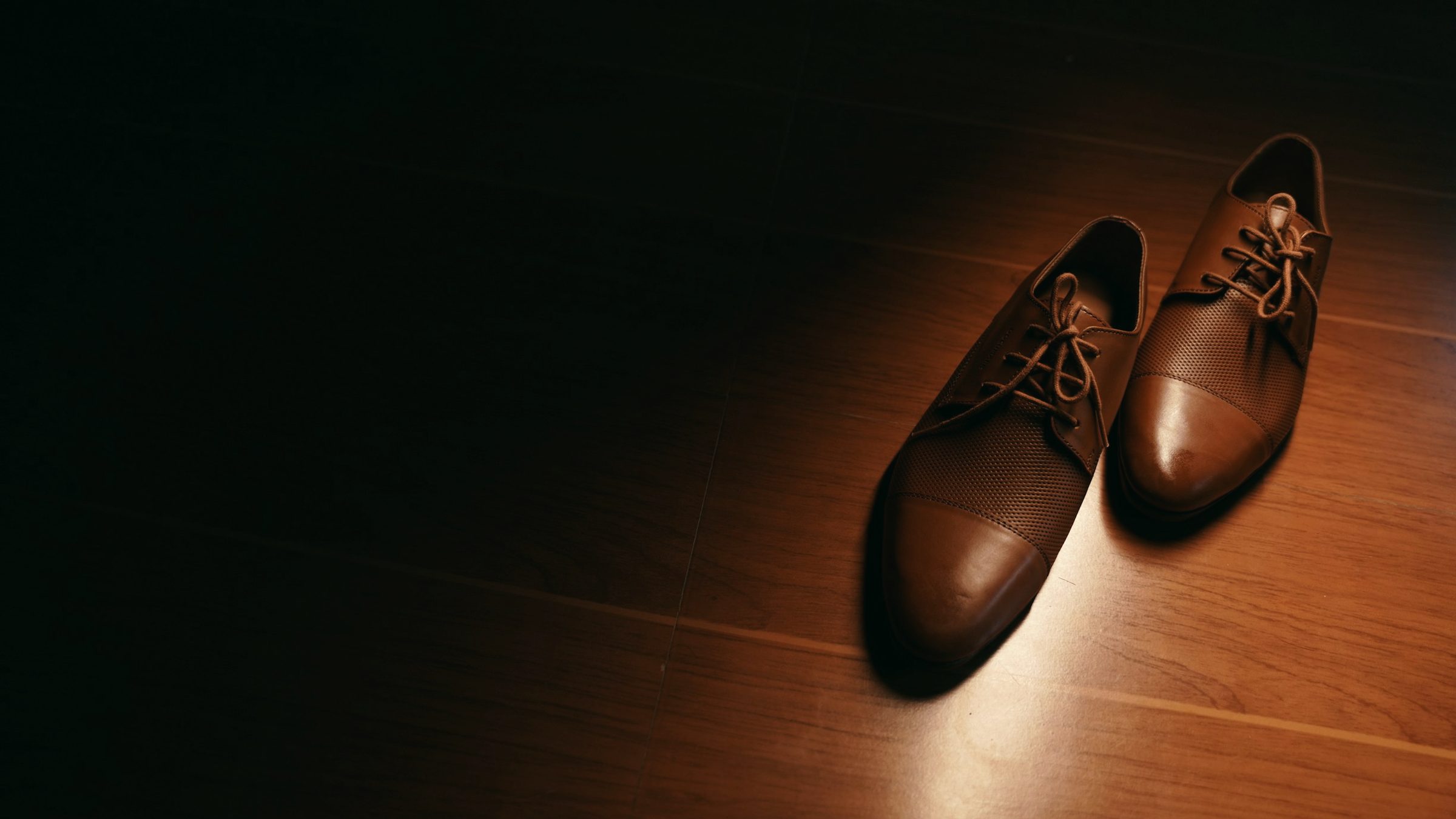 A pair of brown cap-toe leather shoes on a warm wooden floor